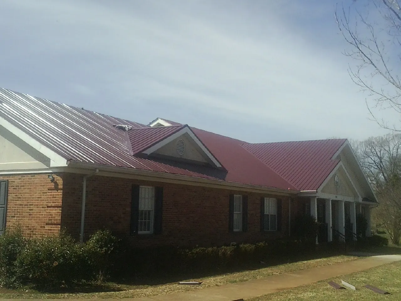 Red metal roof with gabled entries on a long brick building, from a Hail Damage Roof Repair job in Carolina Beach
