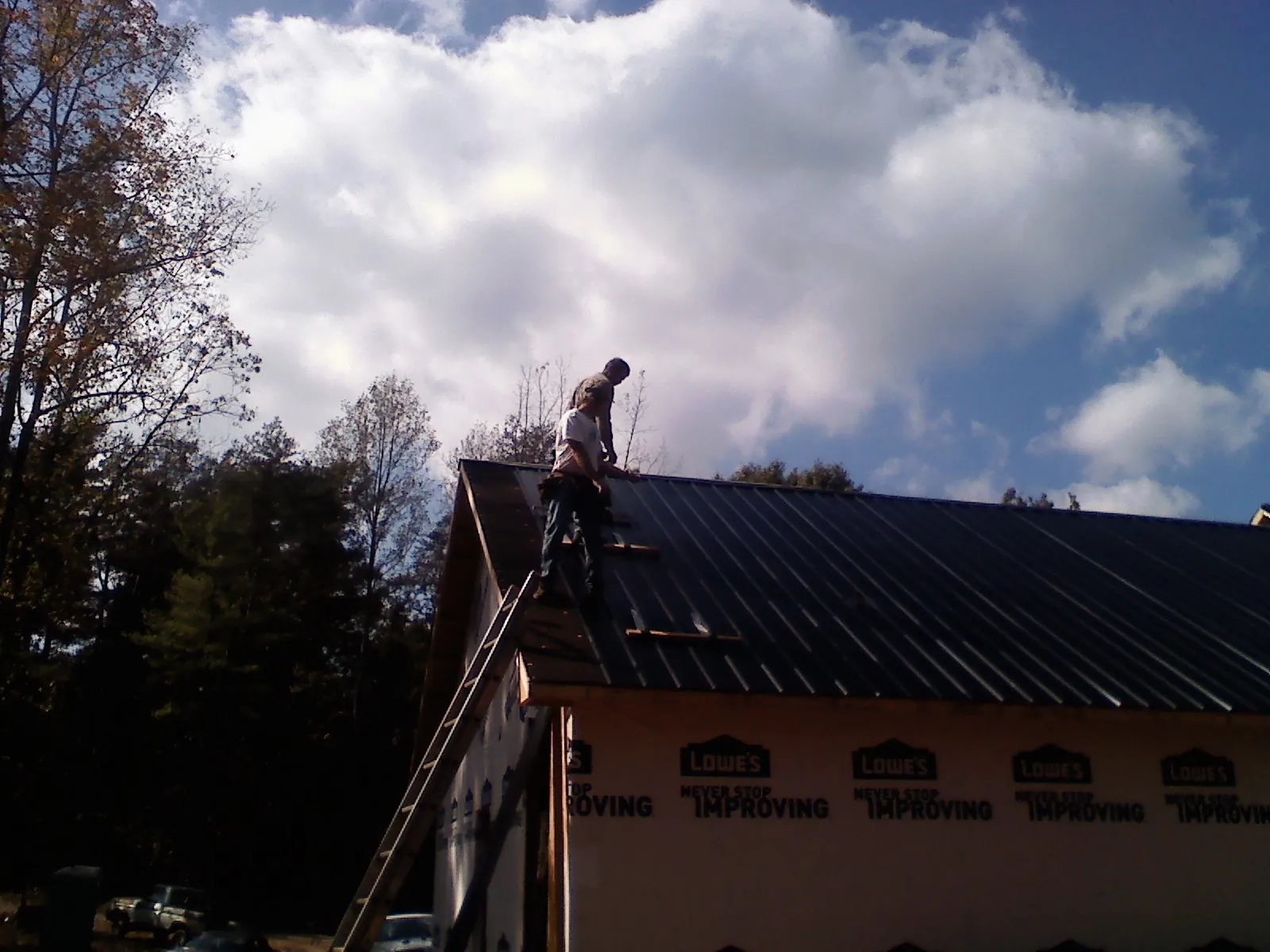 Roofer fastening dark metal panels high against a cloudy sky, from a Roof Inspection job in Carolina Beach