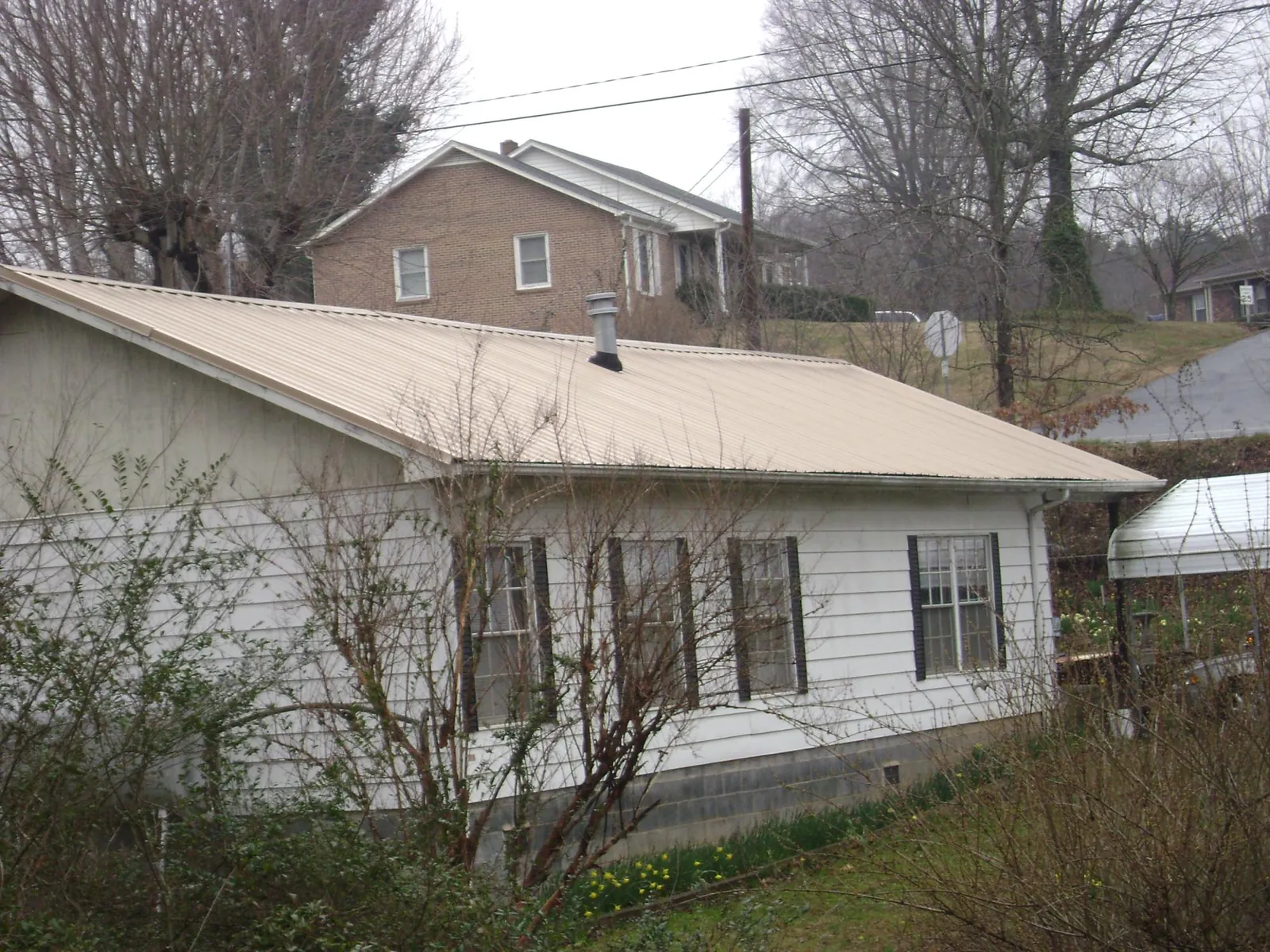 Tan metal roof on a white sided house set into a hillside — Commercial Roofing by Roofing Brothers in Carolina Beach