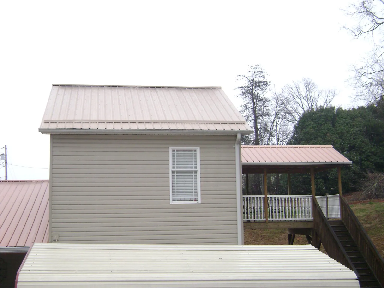 Tan metal roofs on a two story addition and attached porch, from a Roof Replacement job in Carolina Beach